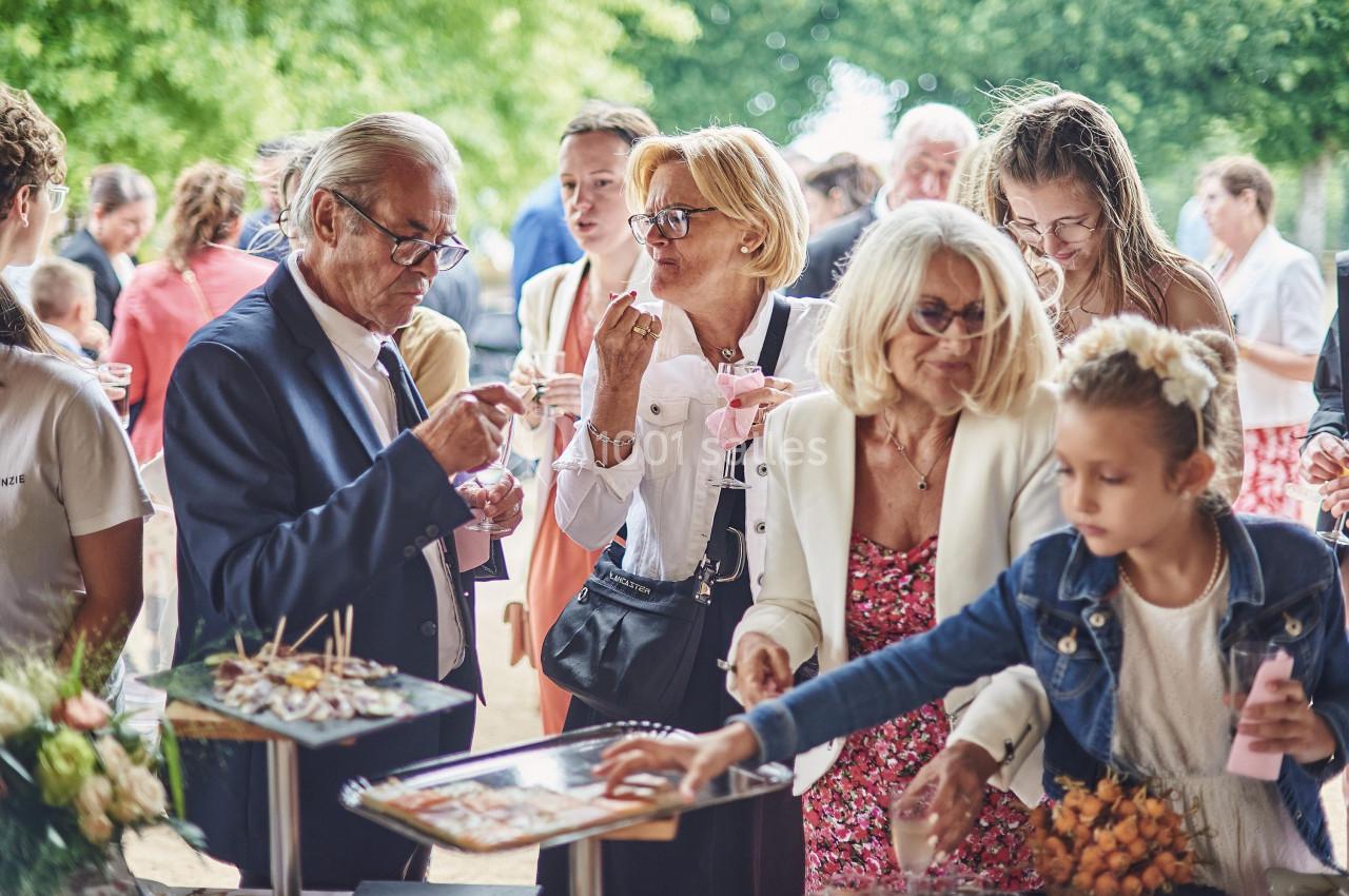 Des personnes de tous âges discutent et se servent à un buffet en extérieur, entourées de verdure.