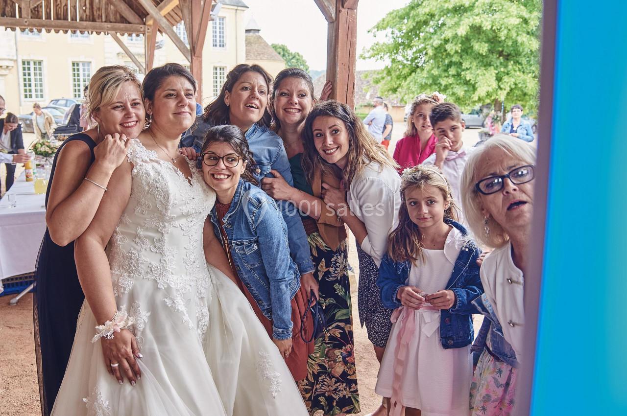 Un groupe de personnes, dont une mariée en robe blanche, pose joyeusement pour une photo lors d'un événement en extérieur.