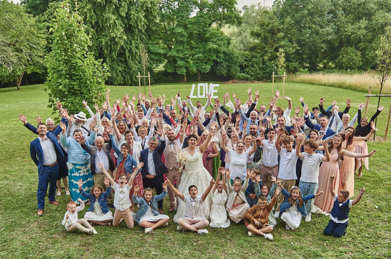 Un grand groupe de personnes souriantes levant les bras, rassemblées dans un parc pour une célébration.