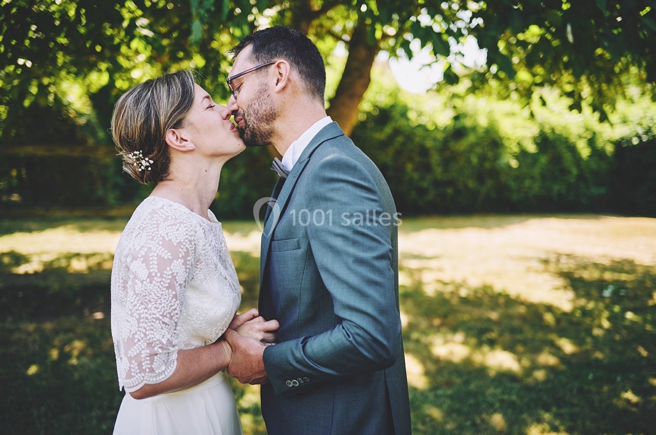 Un couple en tenue de mariage s'embrasse tendrement dans un jardin ensoleillé.