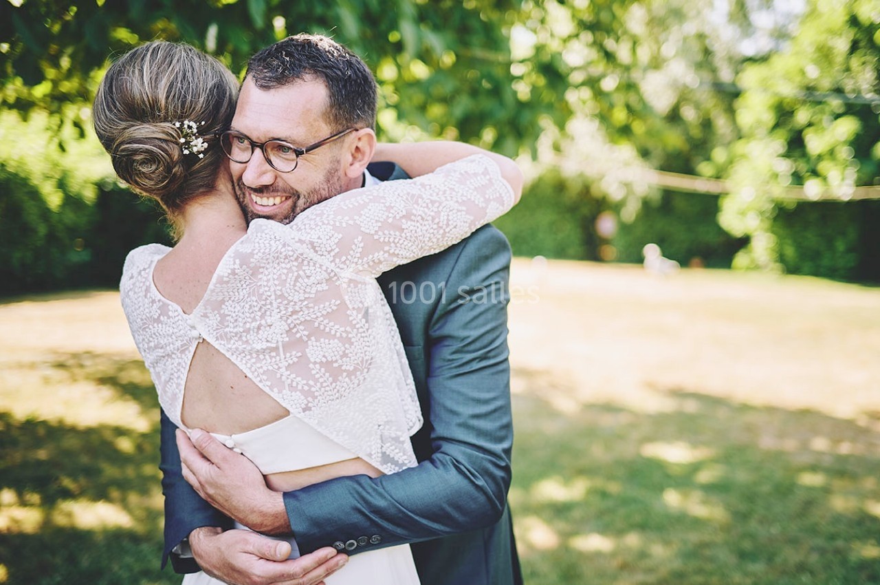 Un couple s'enlace dans un jardin ensoleillé, la femme porte une robe blanche avec un dos en dentelle.