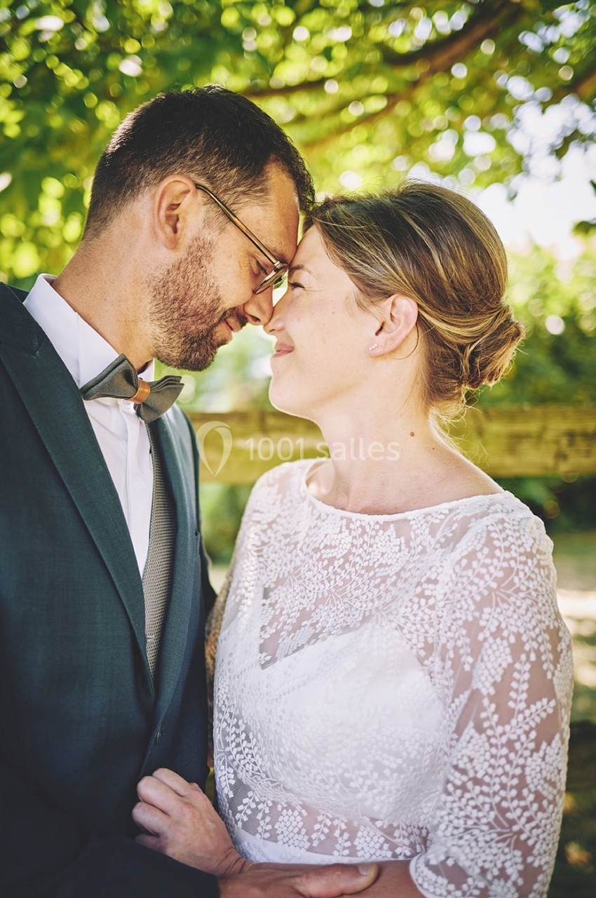 Un couple souriant en tenue de mariage, se tenant tendrement sous des arbres dans un cadre naturel.