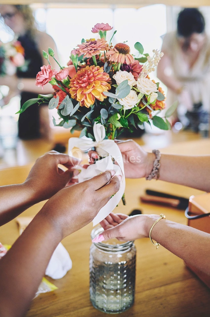 Deux mains attachent un ruban blanc autour d'un bouquet de fleurs colorées posé sur une table en bois.