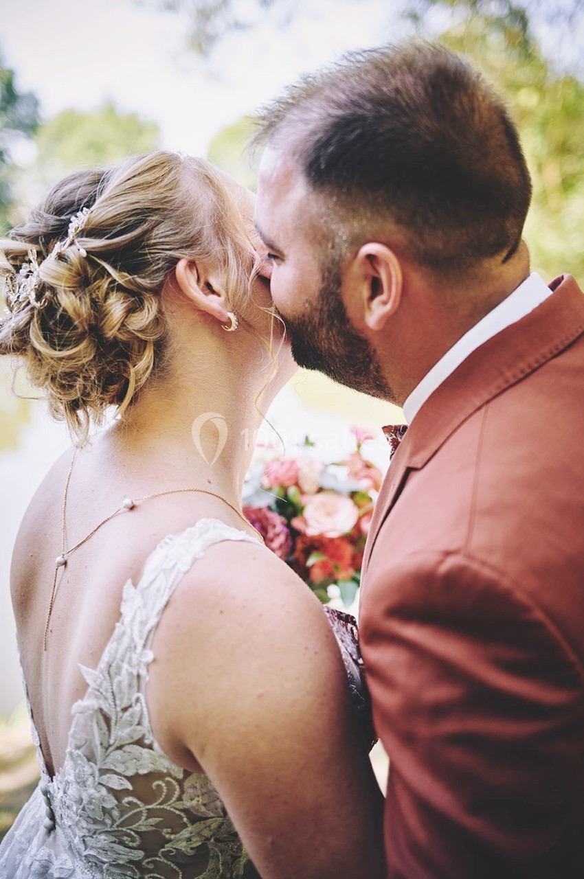 Un couple s'embrasse tendrement en extérieur, la femme porte une robe blanche et l'homme un costume rouge.