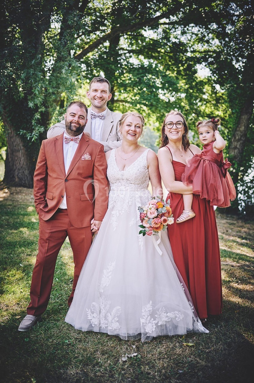 Un groupe de cinq personnes posant en tenue de mariage dans un parc verdoyant.