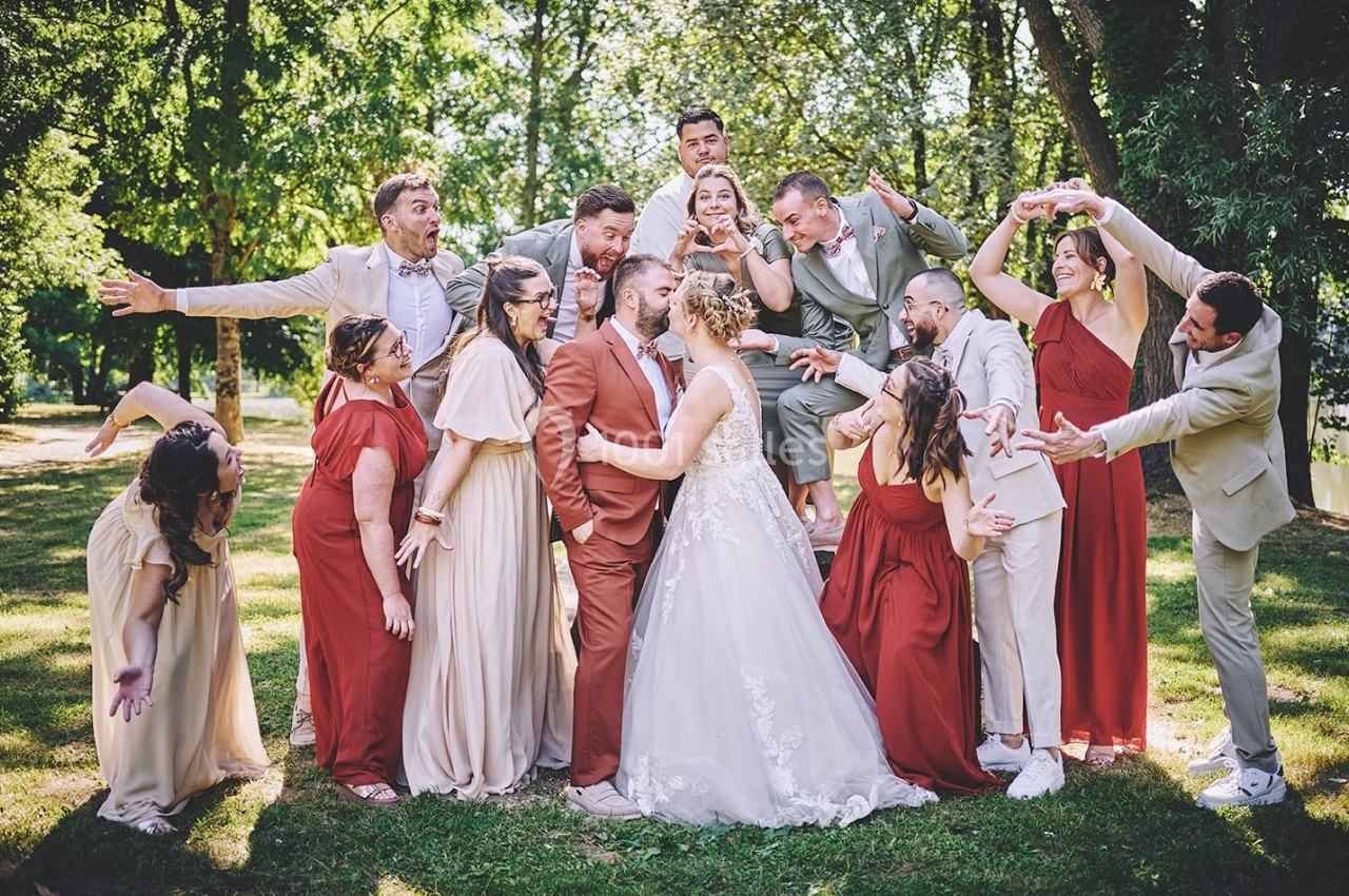Un couple de mariés entouré de leurs invités en tenues élégantes, posant de manière joyeuse dans un parc verdoyant.