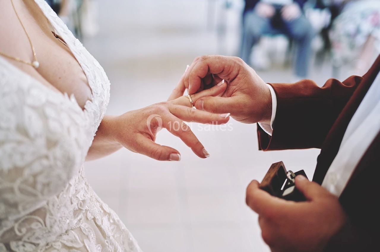 Un homme passe une alliance au doigt d'une femme vêtue d'une robe blanche lors d'une cérémonie.