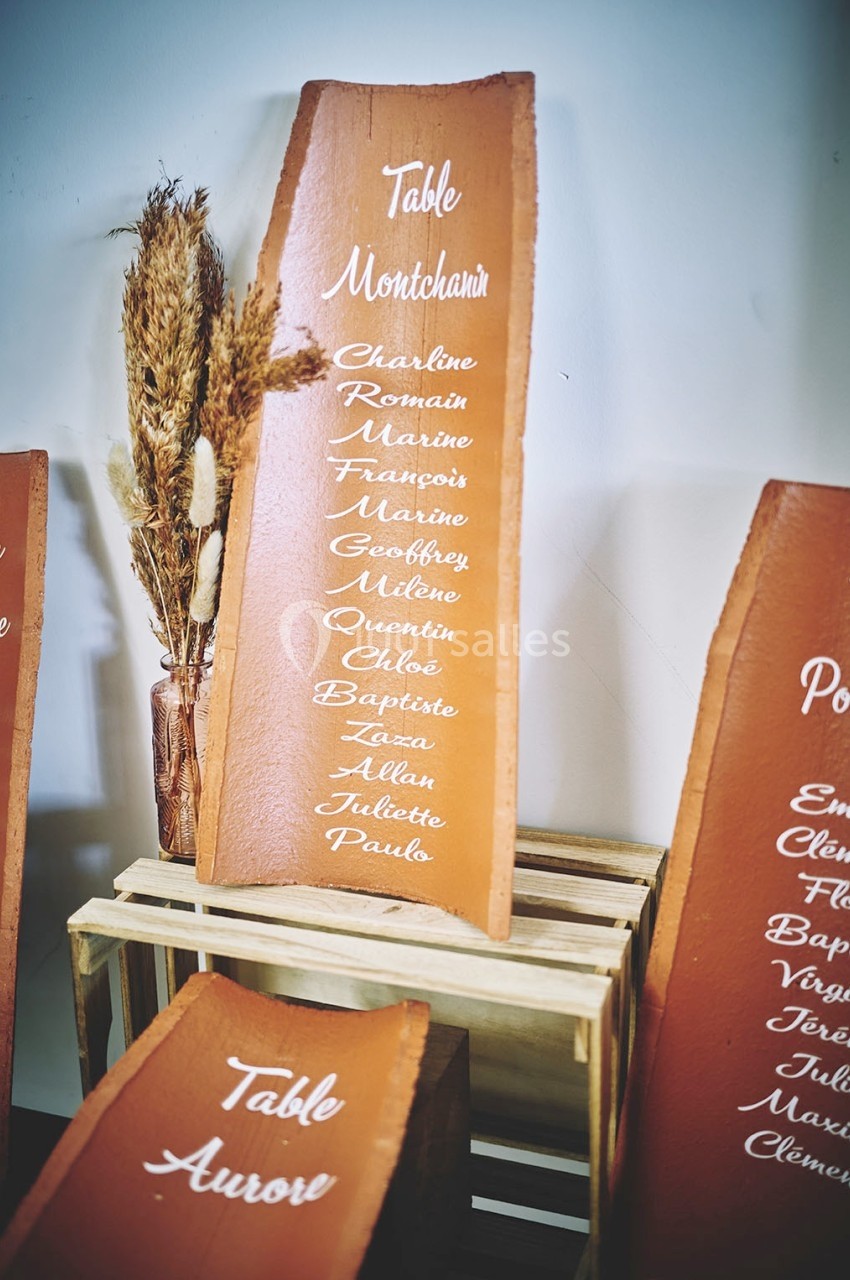 Liste de prénoms manuscrits sur une plaque en bois, posée sur un support avec des épis de blé en décoration.