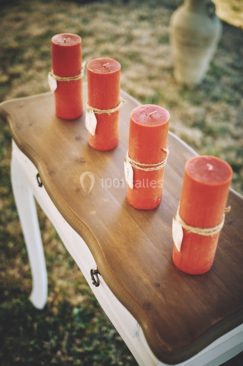 Quatre bougies rouges attachées avec de la ficelle sont alignées sur une petite table en bois dans un espace extérieur.