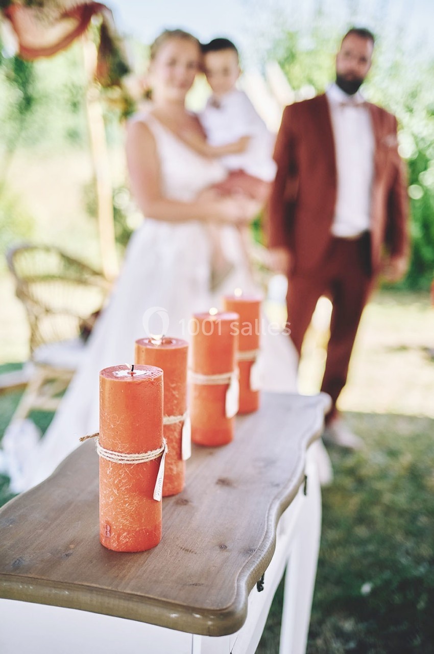 Quatre bougies rouges décoratives posées sur une table en bois, avec un couple et un enfant flous en arrière-plan.