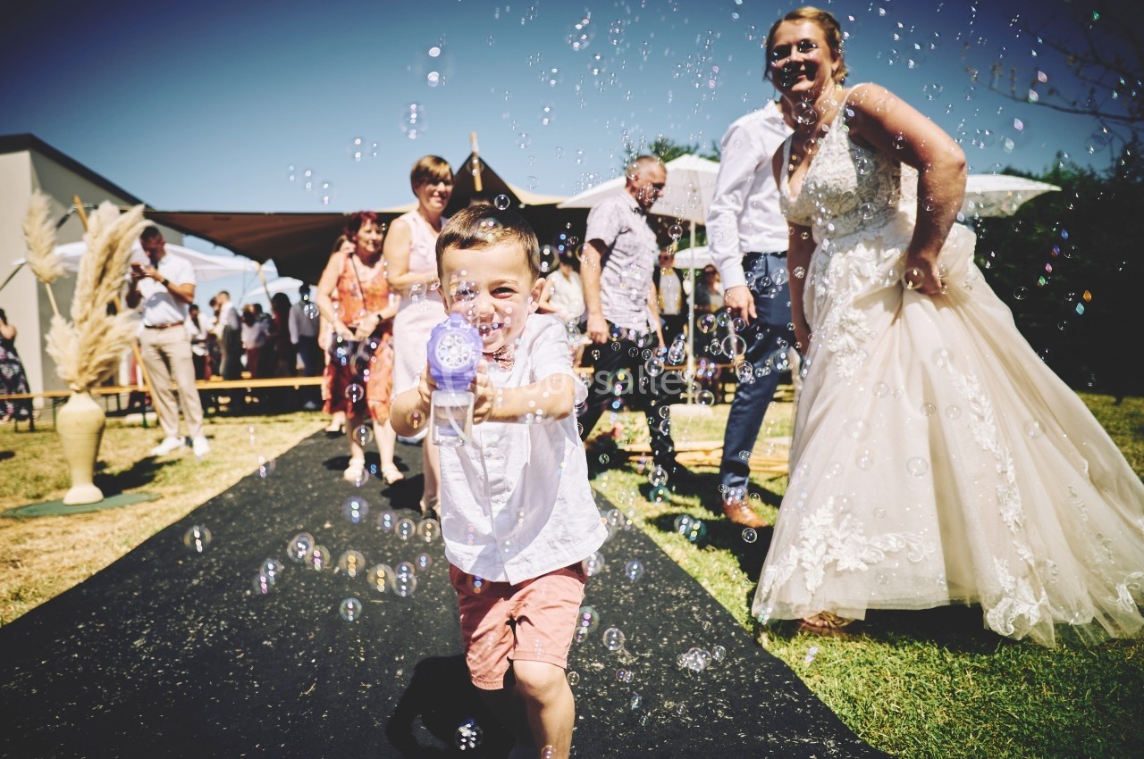 Un enfant joue avec un pistolet à bulles sur une allée extérieure lors d'un événement festif en plein air.