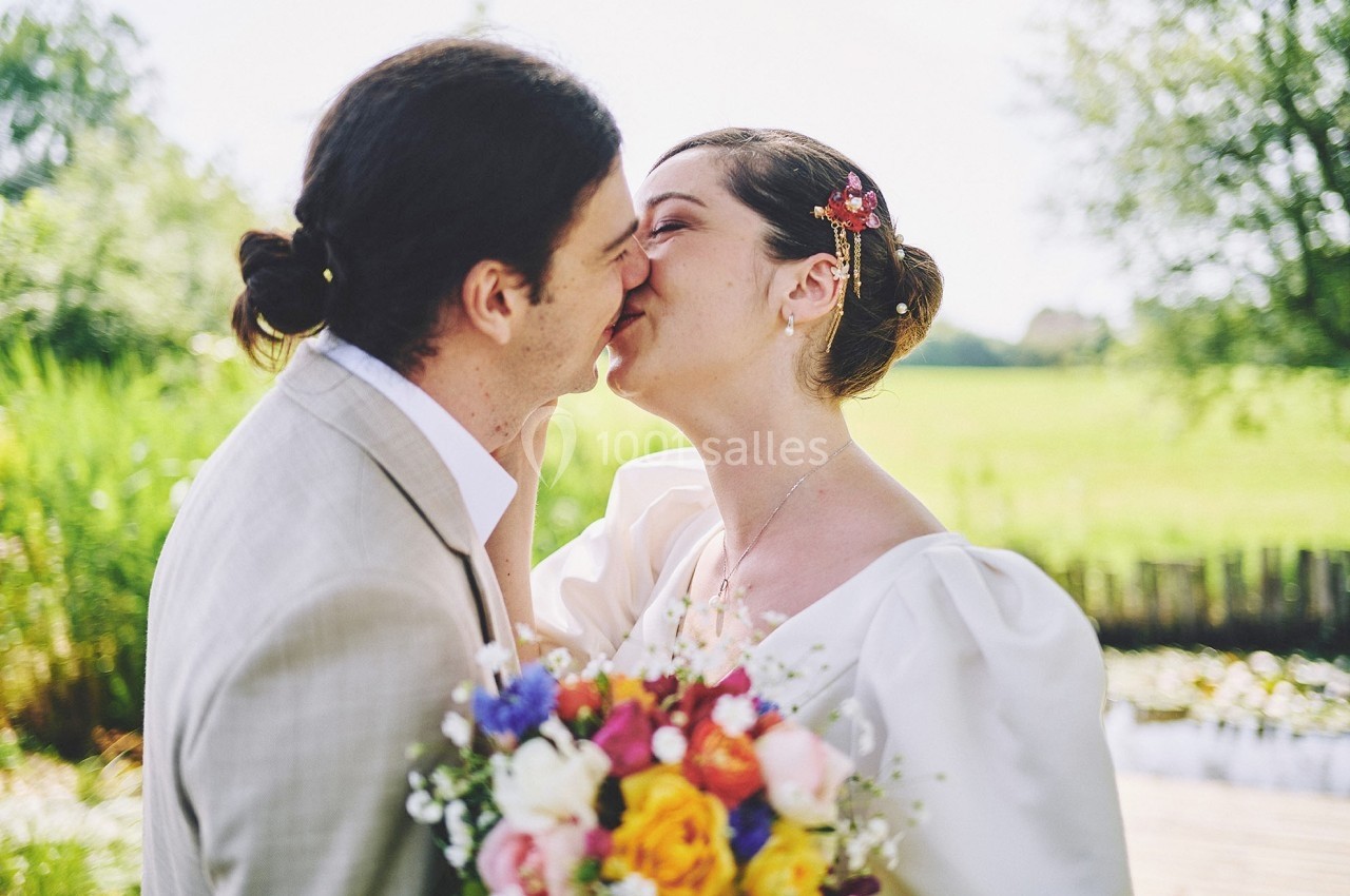 Un couple s'embrasse en extérieur, la mariée tenant un bouquet coloré devant un paysage verdoyant.