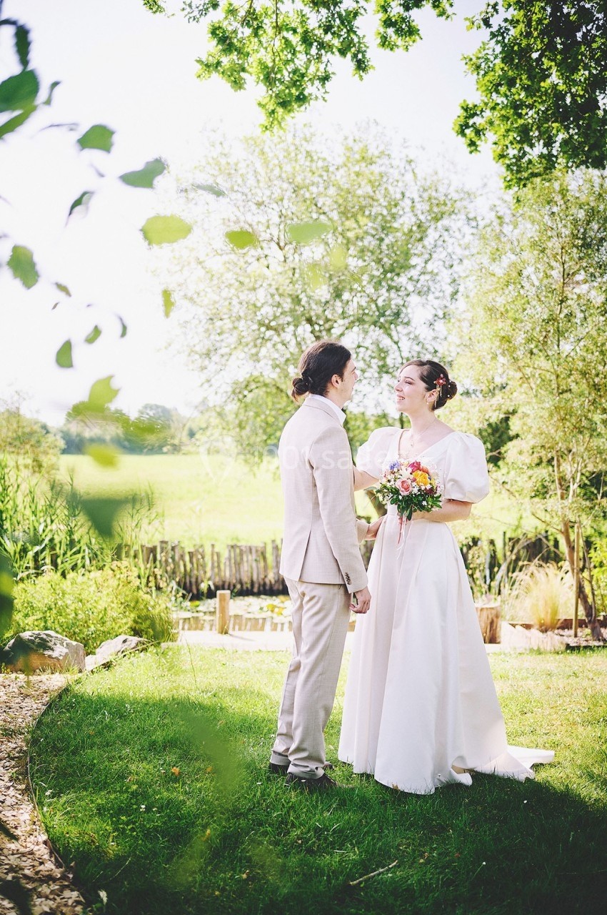 Un couple en tenue de mariage se tient debout dans un jardin verdoyant par une journée ensoleillée.