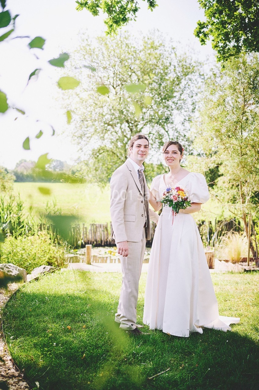 Un couple en tenue de mariage pose dans un jardin verdoyant par une journée ensoleillée.