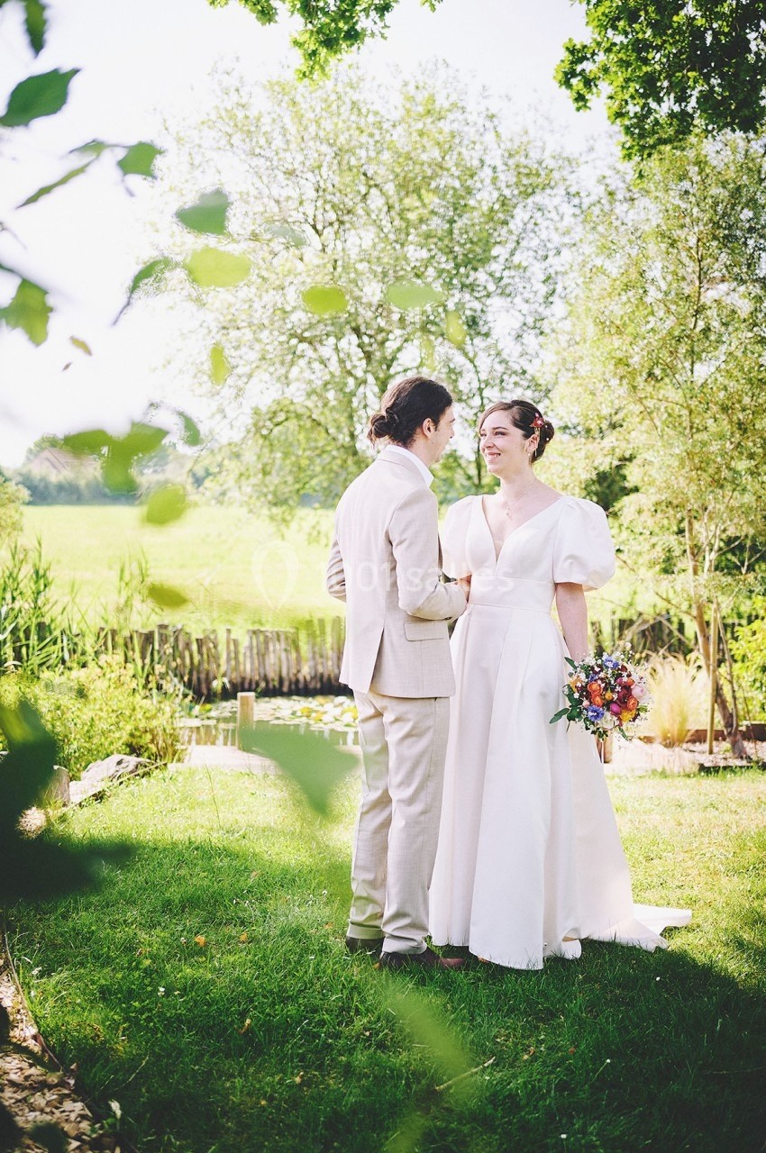 Un couple en tenue de mariage se tient dans un jardin verdoyant, la mariée tenant un bouquet coloré.
