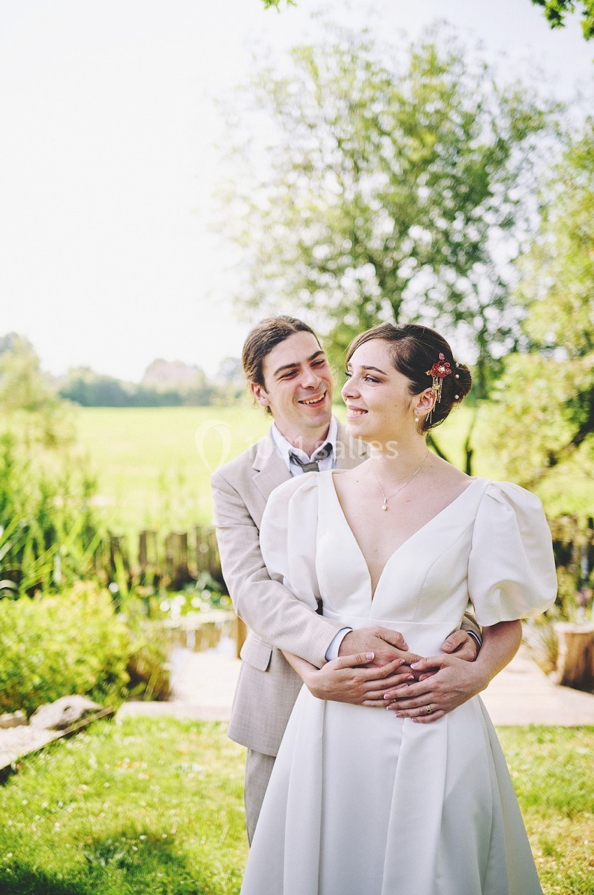 Un couple en tenue de mariage pose dans un jardin verdoyant par une journée ensoleillée.