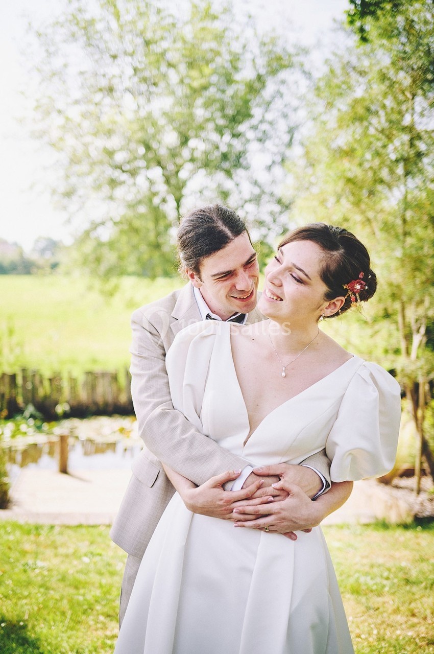 Un couple en tenue de mariage s'enlace dans un jardin verdoyant par une journée ensoleillée.