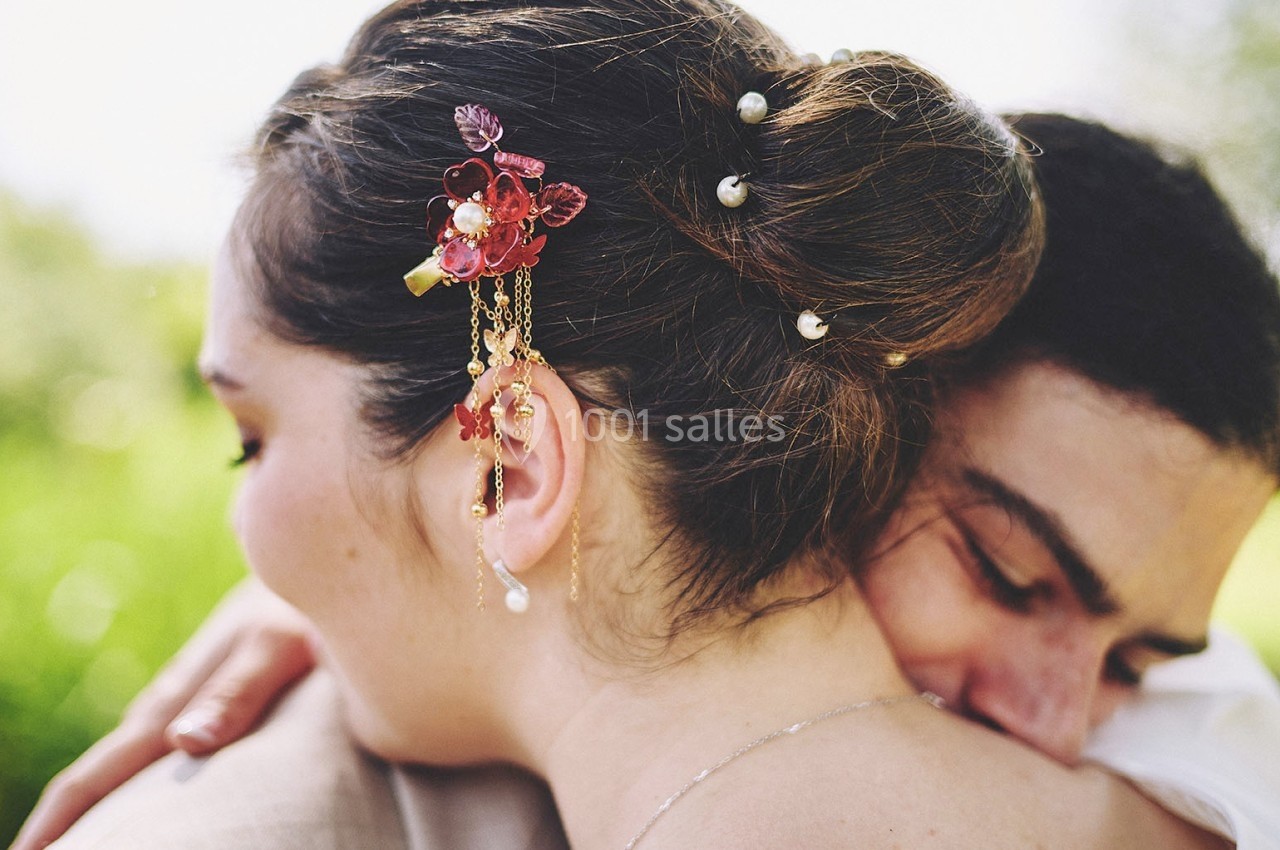 Une femme portant un bijou floral dans les cheveux est enlacée par un homme dans un cadre extérieur lumineux.