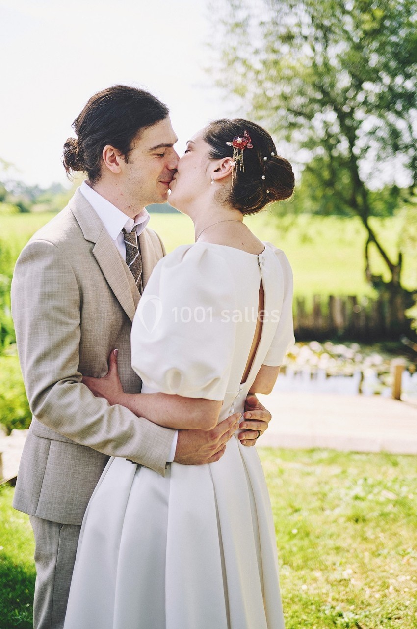 Un couple en tenue de mariage s'embrasse tendrement dans un jardin verdoyant près d'un étang.