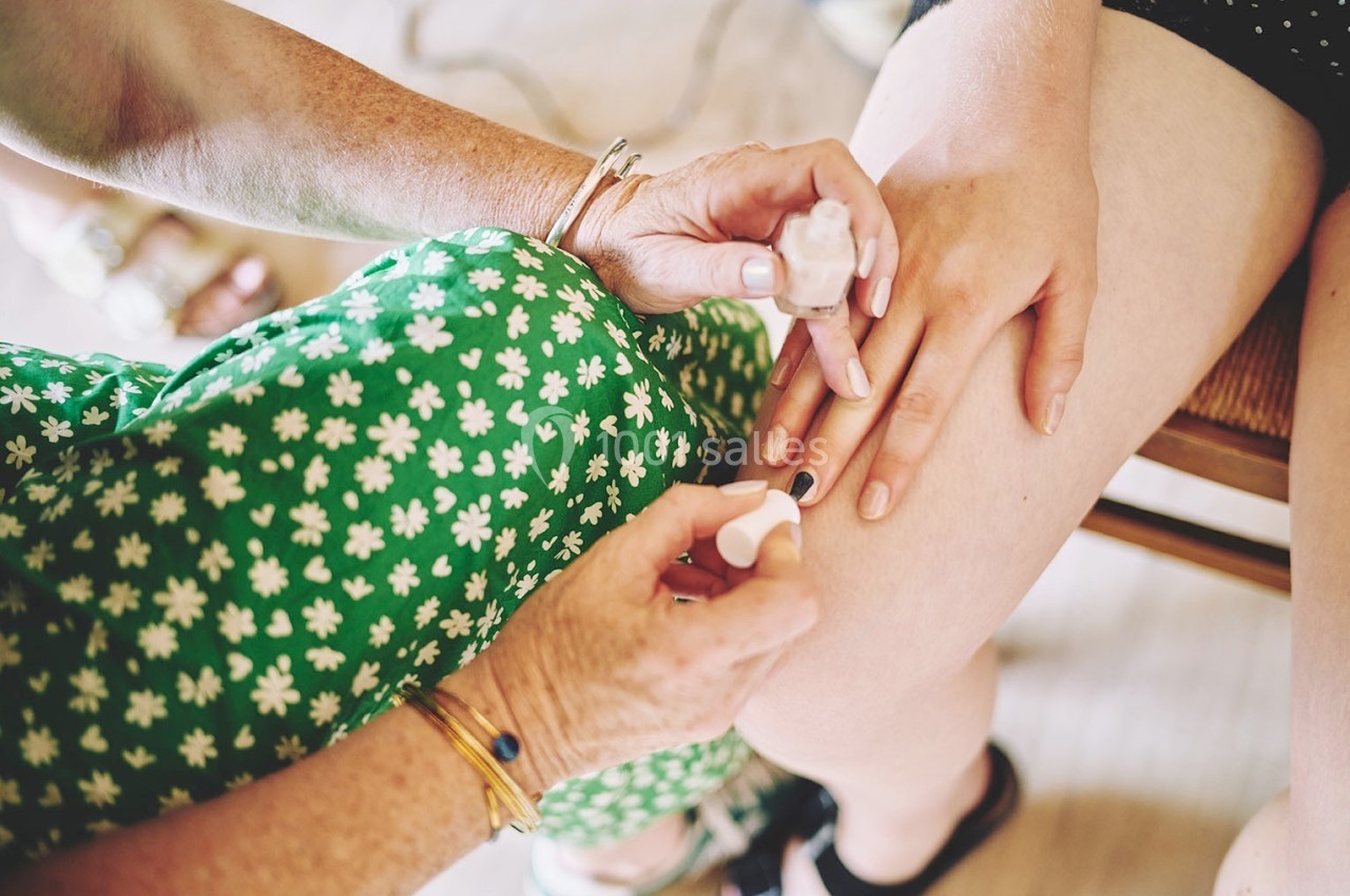 Une personne applique du vernis à ongles sur la main d'une autre, assise, portant une robe verte à motifs floraux.