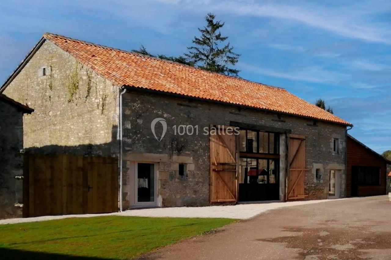 Bâtiment en pierre rénové avec toit en tuiles, grandes portes en bois ouvertes et fenêtres modernes.