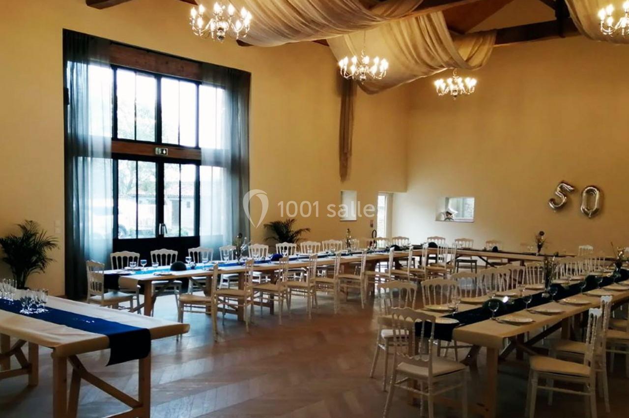 Salle de réception décorée avec des tables alignées, nappes bleues, chaises blanches et ballons formant le chiffre 50.