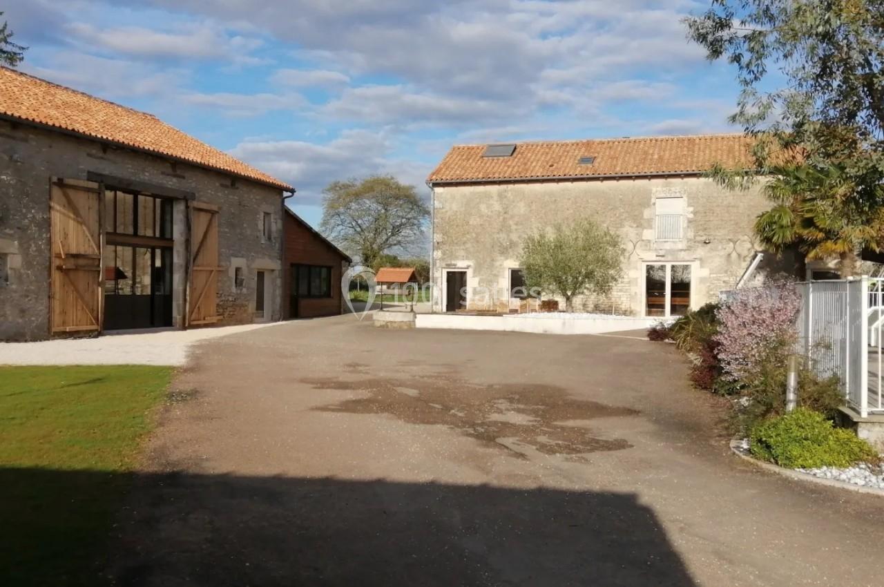 Cour extérieure avec bâtiments en pierre, toits en tuiles, arbres et ciel partiellement nuageux.