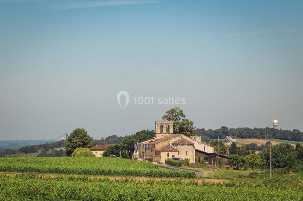 Vue d'un village rural avec une église en pierre entourée de champs verdoyants sous un ciel dégagé.