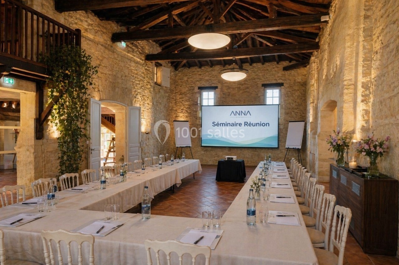 Salle de séminaire lumineuse avec tables disposées en U, écran de projection, chevalets et murs en pierre apparente.