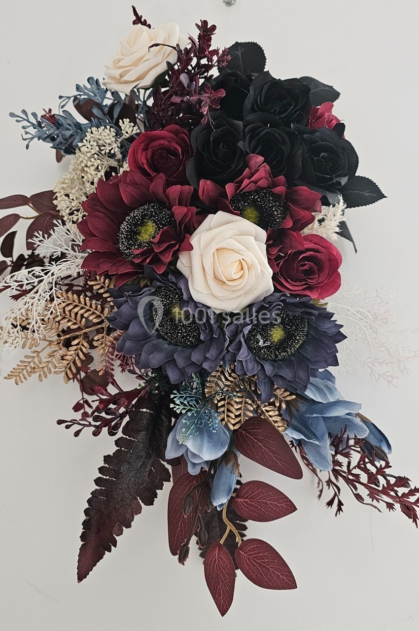 Composition florale avec roses rouges, blanches et noires, fleurs violettes et feuillage décoratif sur fond clair.