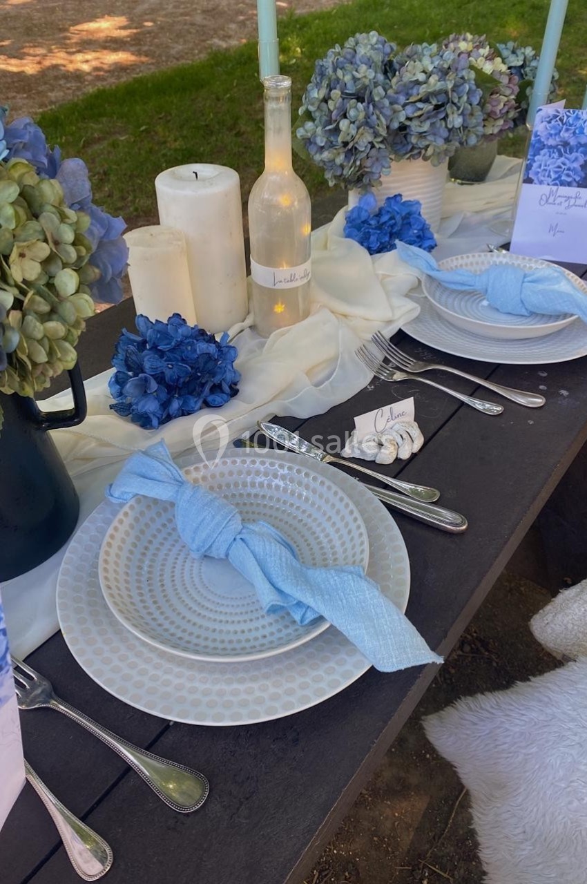 Table décorée avec des assiettes blanches, serviettes bleues, bougies et bouquets d'hortensias bleus et blancs.