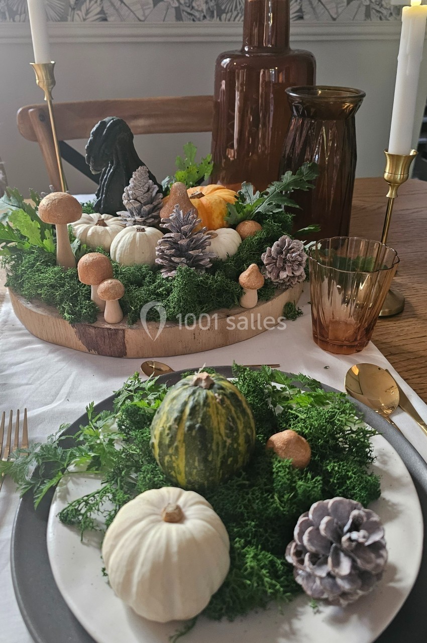 Décoration de table automnale avec citrouilles, mousse, pommes de pin et bougies dans une ambiance chaleureuse.