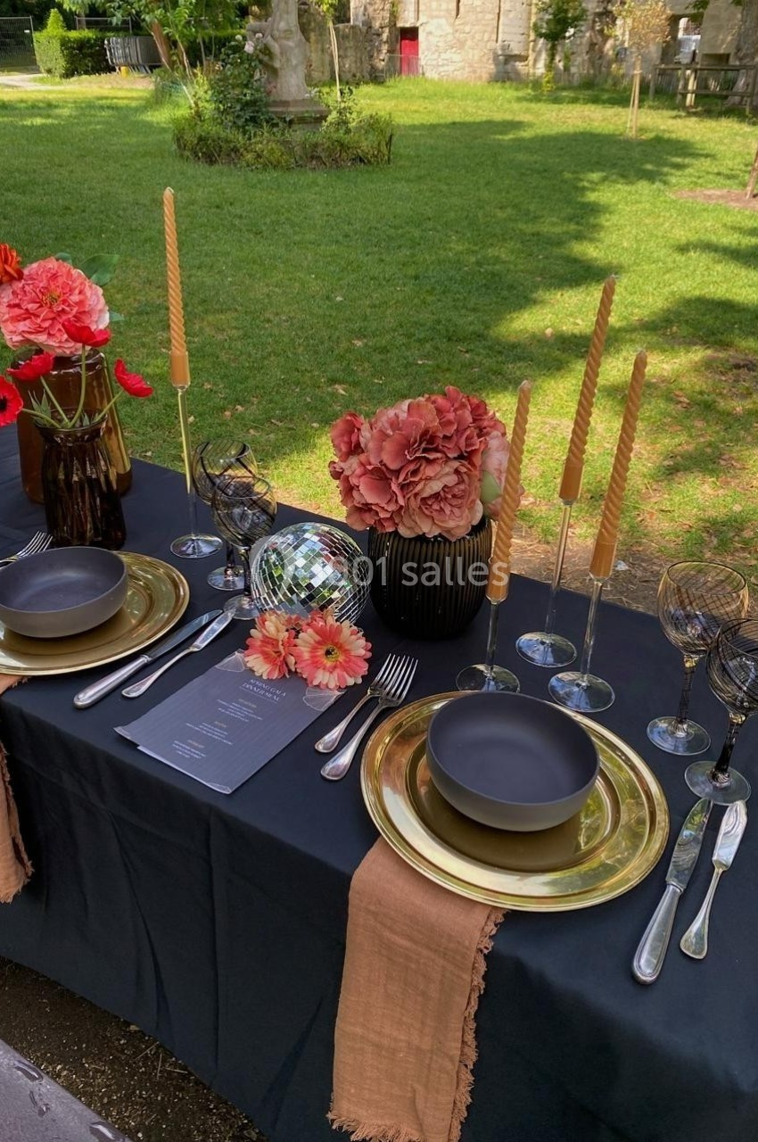 Table élégamment dressée en extérieur avec vaisselle noire, fleurs colorées, bougies torsadées et une boule disco.
