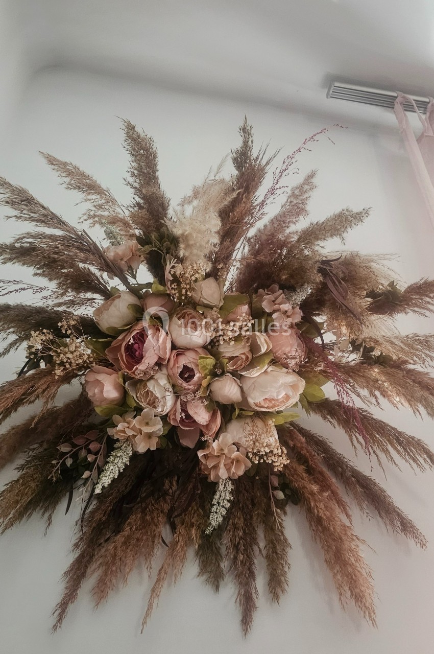 Composition florale suspendue avec des fleurs séchées, des pampas et des roses dans des tons naturels et pastel.