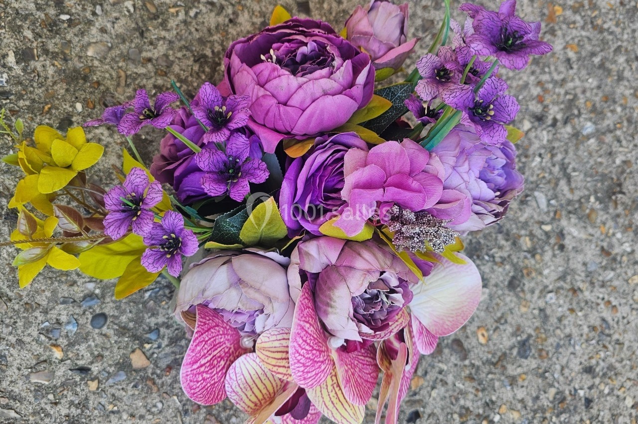 Bouquet de fleurs violettes et roses avec des touches de jaune, posé sur un sol en béton granuleux.