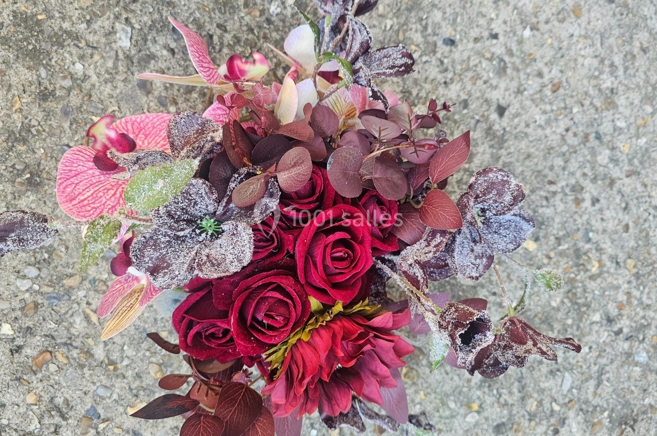 Bouquet de fleurs rouges et roses avec feuillage texturé, posé sur un sol gris granuleux.