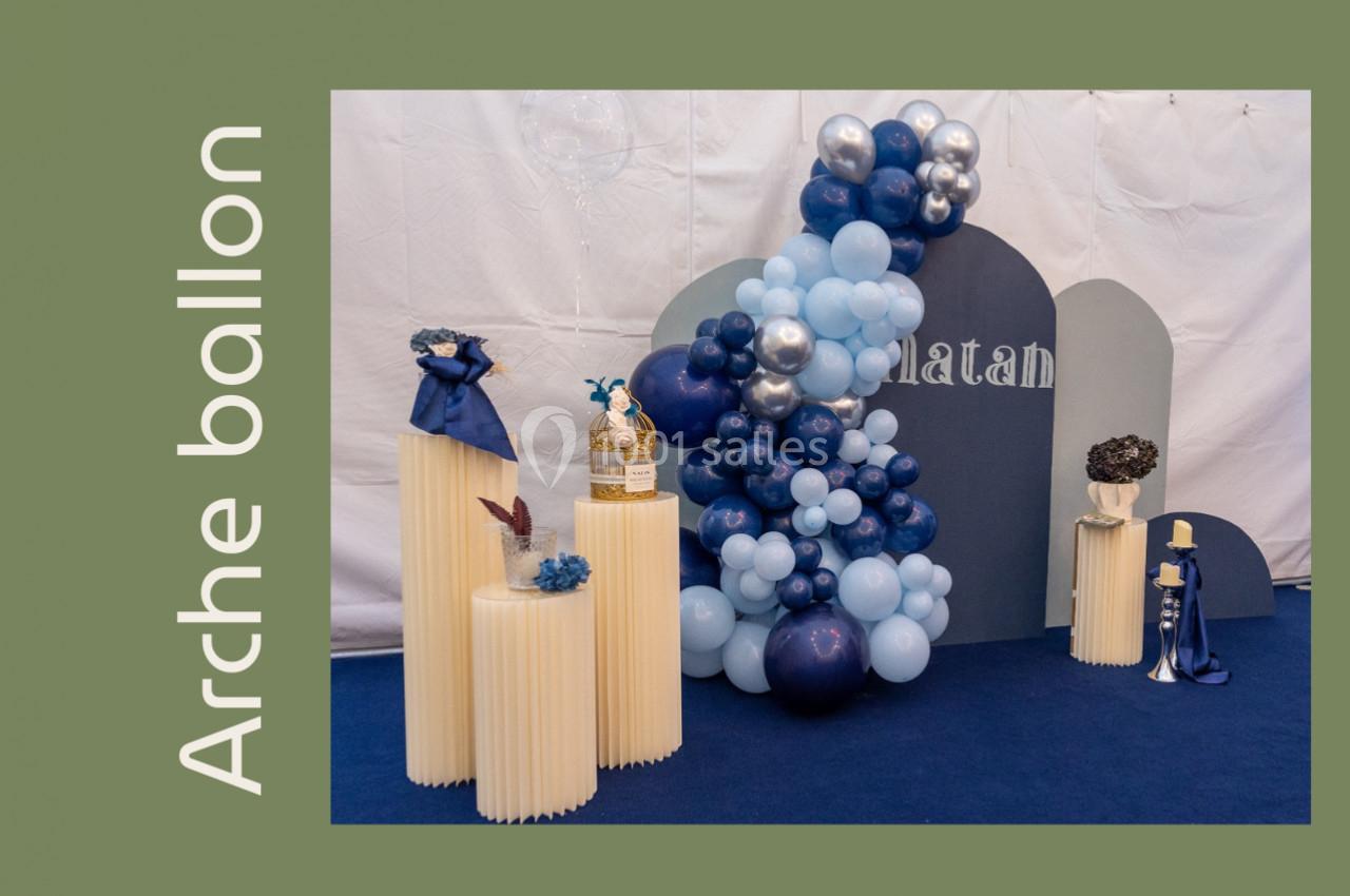 Décoration avec arche de ballons bleus et argentés, présentoirs blancs et accessoires sur fond bleu et blanc.