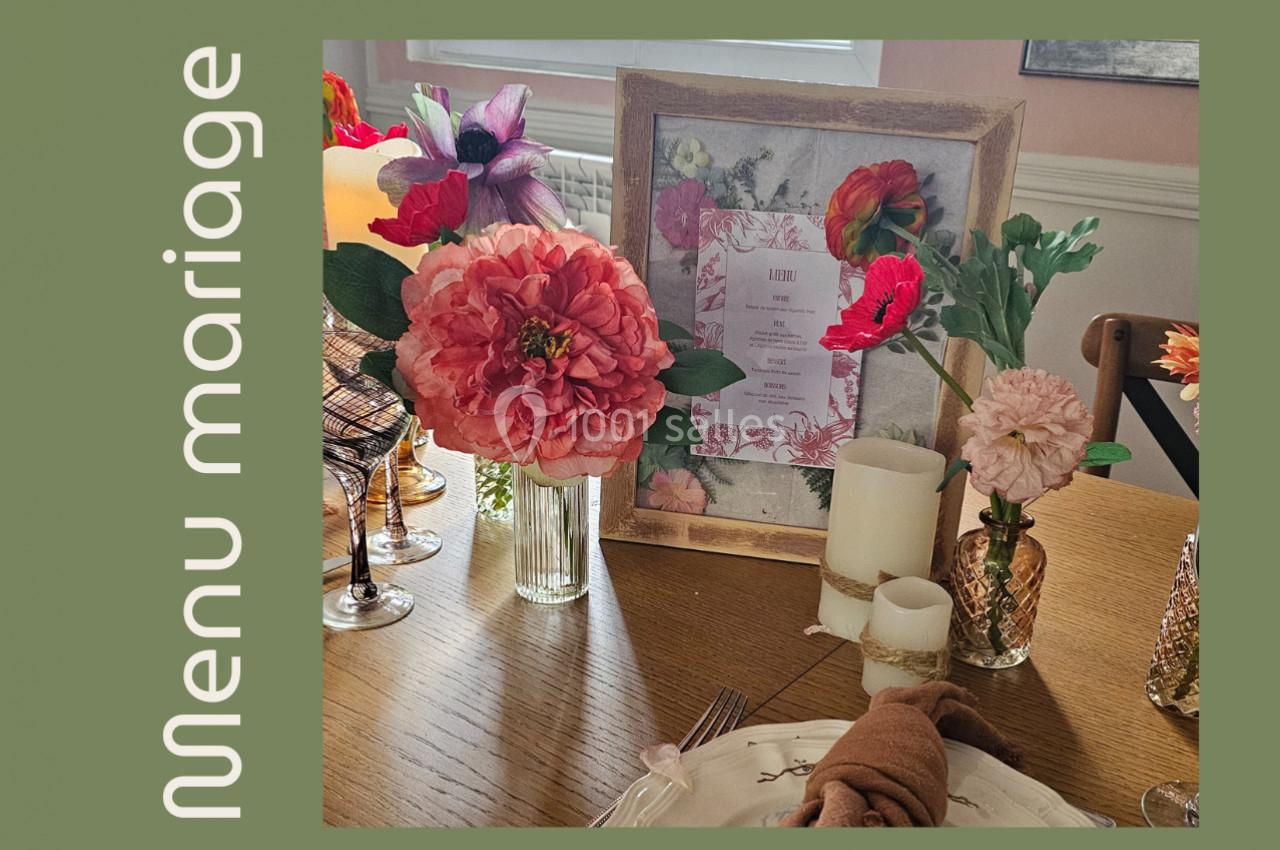 Décoration de table avec fleurs colorées, menu encadré et bougies sur une nappe en bois.