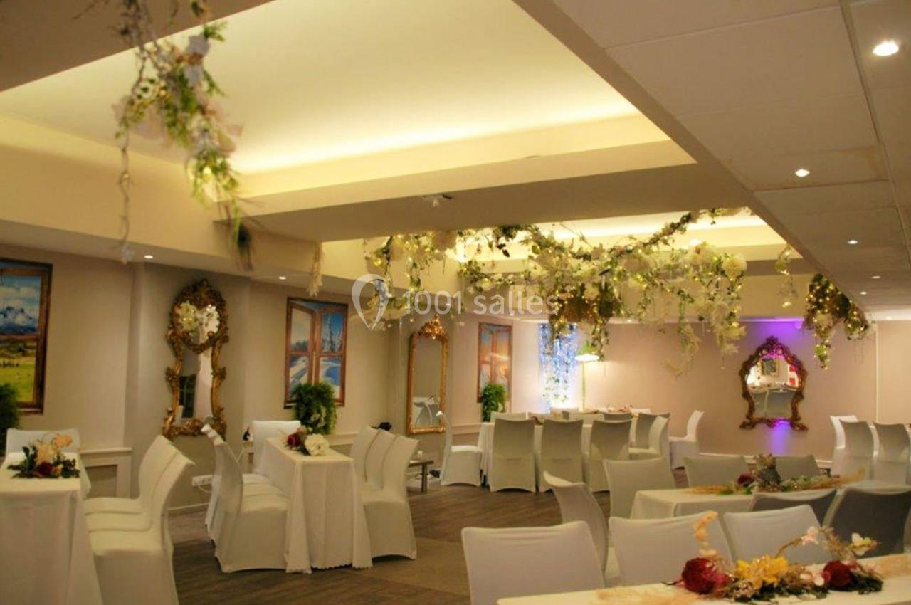 Salle de réception décorée avec des guirlandes florales suspendues, tables dressées et miroirs ornés sur les murs.
