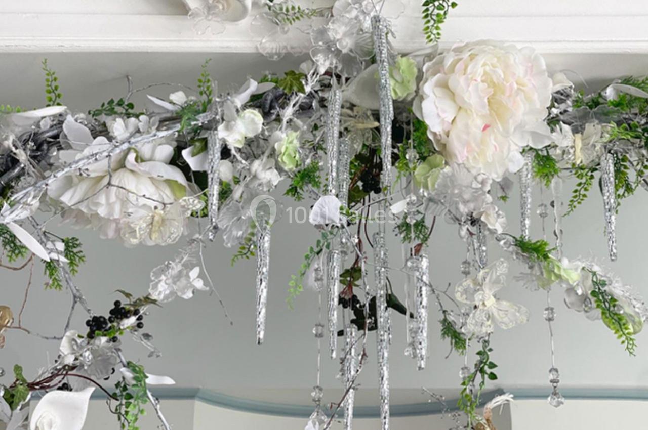 Guirlande décorative composée de fleurs blanches, feuillages verts et ornements argentés suspendus.