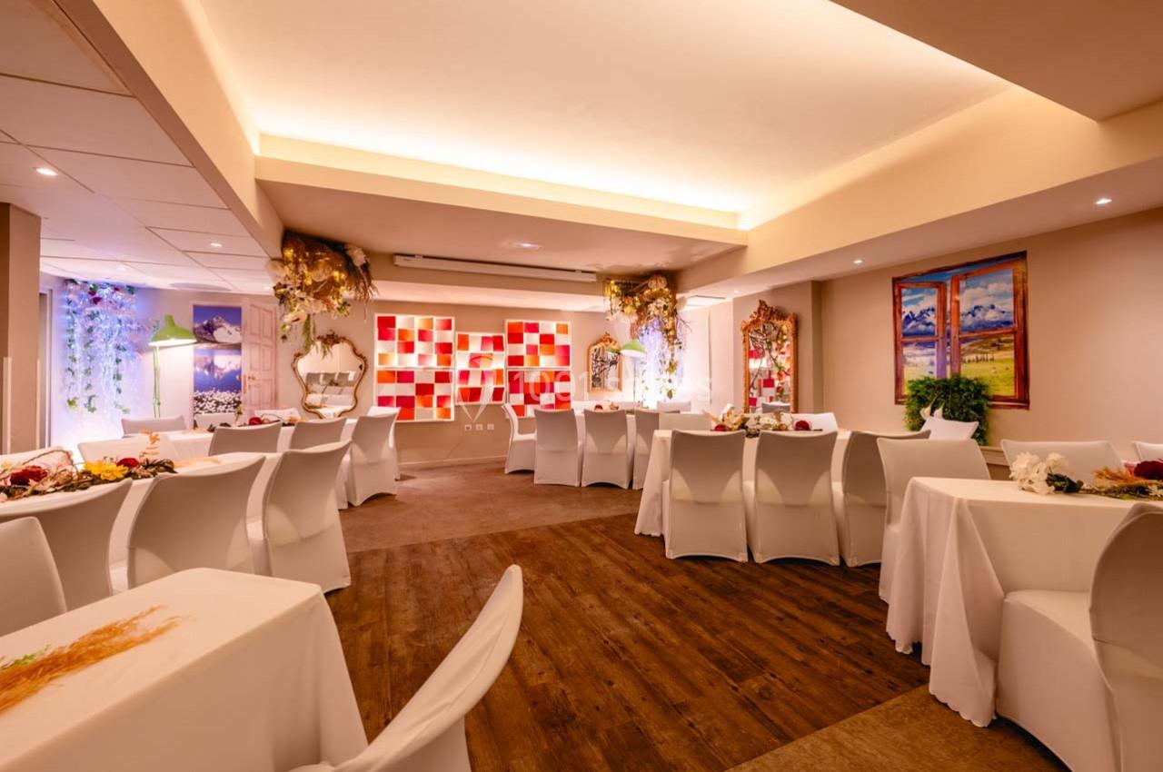 Salle de réception lumineuse avec tables dressées, chaises blanches et décorations murales colorées.