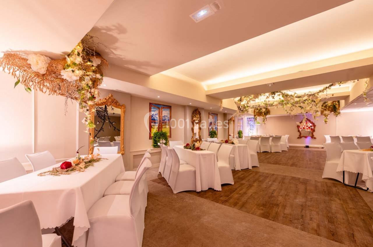 Salle de réception décorée avec des tables blanches, des chaises assorties et des ornements floraux suspendus.