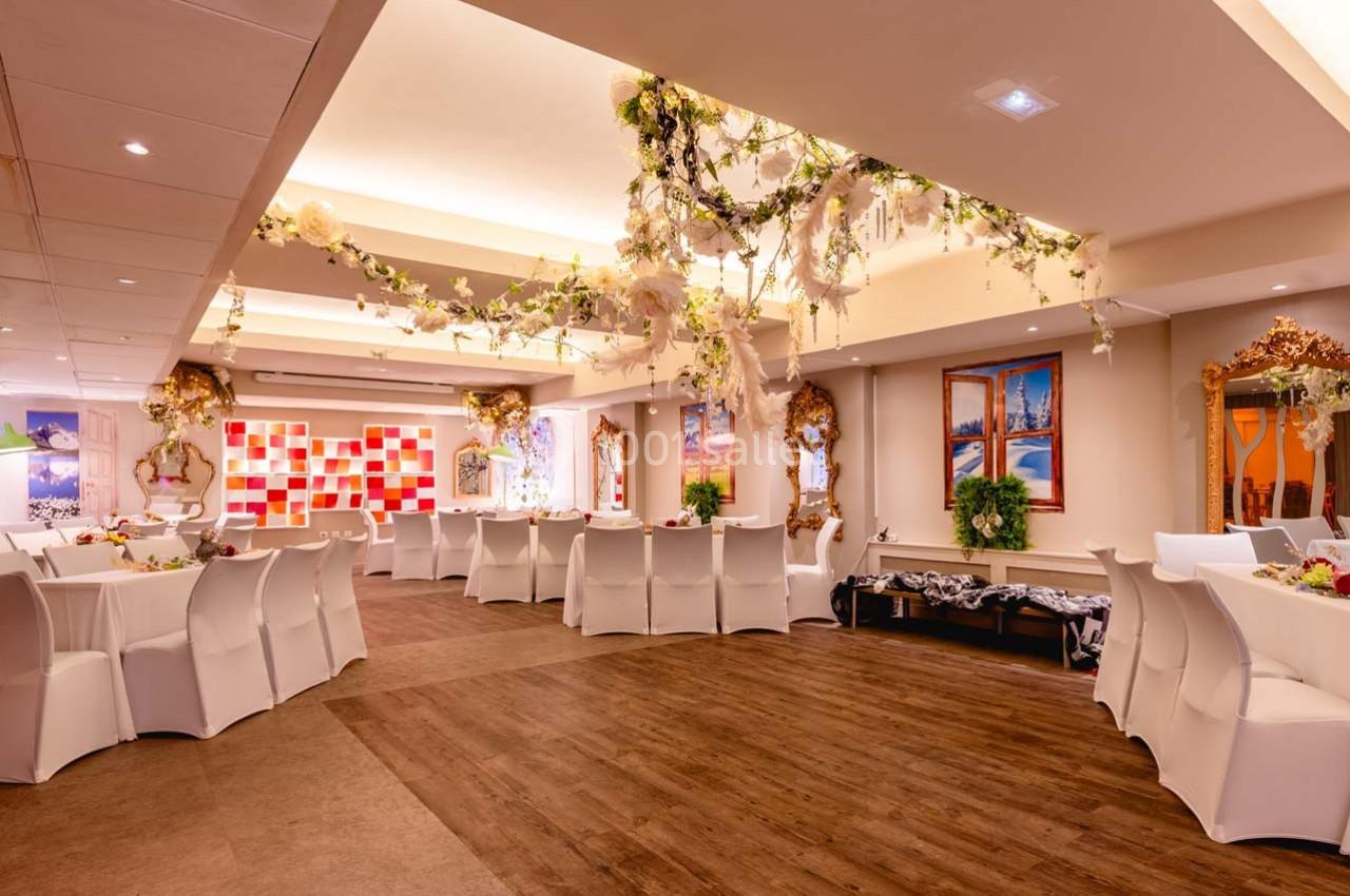 Salle de réception décorée avec des fleurs suspendues, des tables rondes dressées et un sol en bois.
