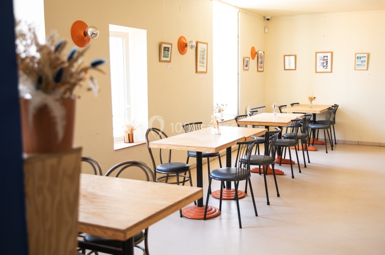Salle lumineuse avec des tables en bois, des chaises noires et des décorations murales colorées.
