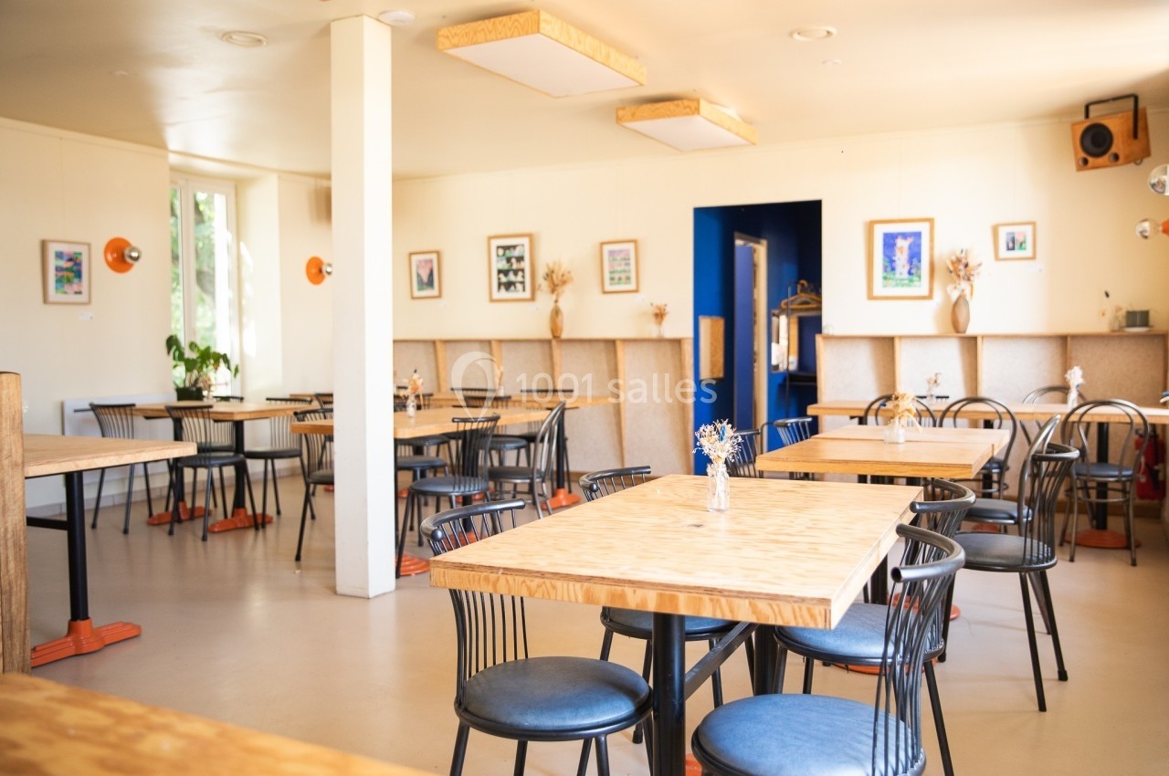 Salle de restaurant lumineuse avec tables en bois, chaises noires et décorations murales colorées.