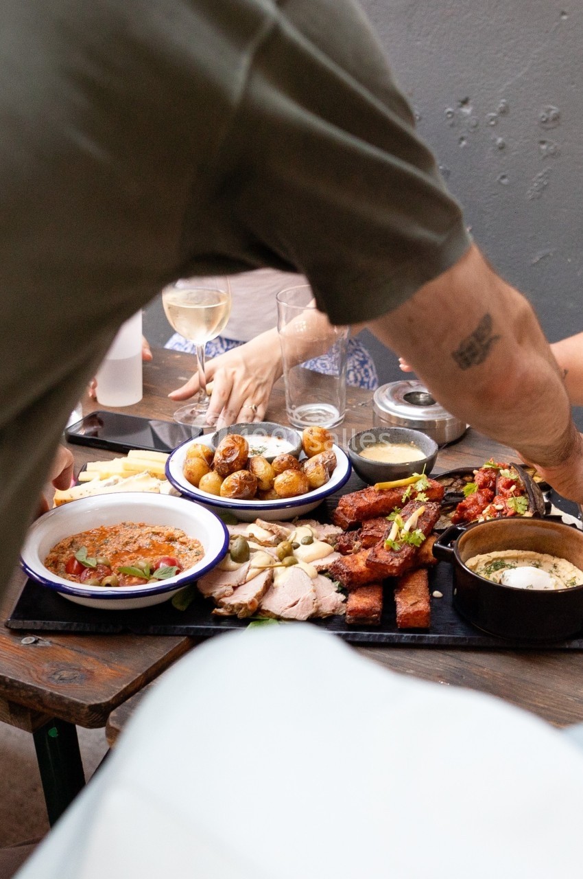 Un groupe partage un repas composé de viande, pommes de terre et accompagnements sur une table en extérieur.
