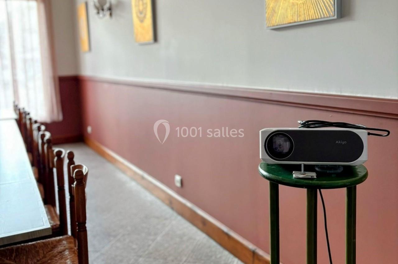 Projecteur posé sur un tabouret vert dans une pièce avec des murs bicolores et des tableaux accrochés.