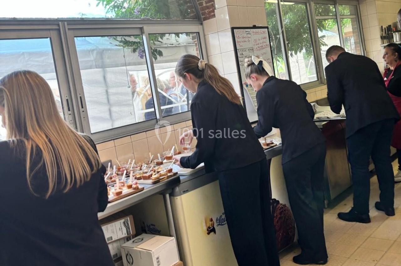 Des serveurs en tenue professionnelle préparent des amuse-bouches dans une cuisine lumineuse avec vue sur l'extérieur.