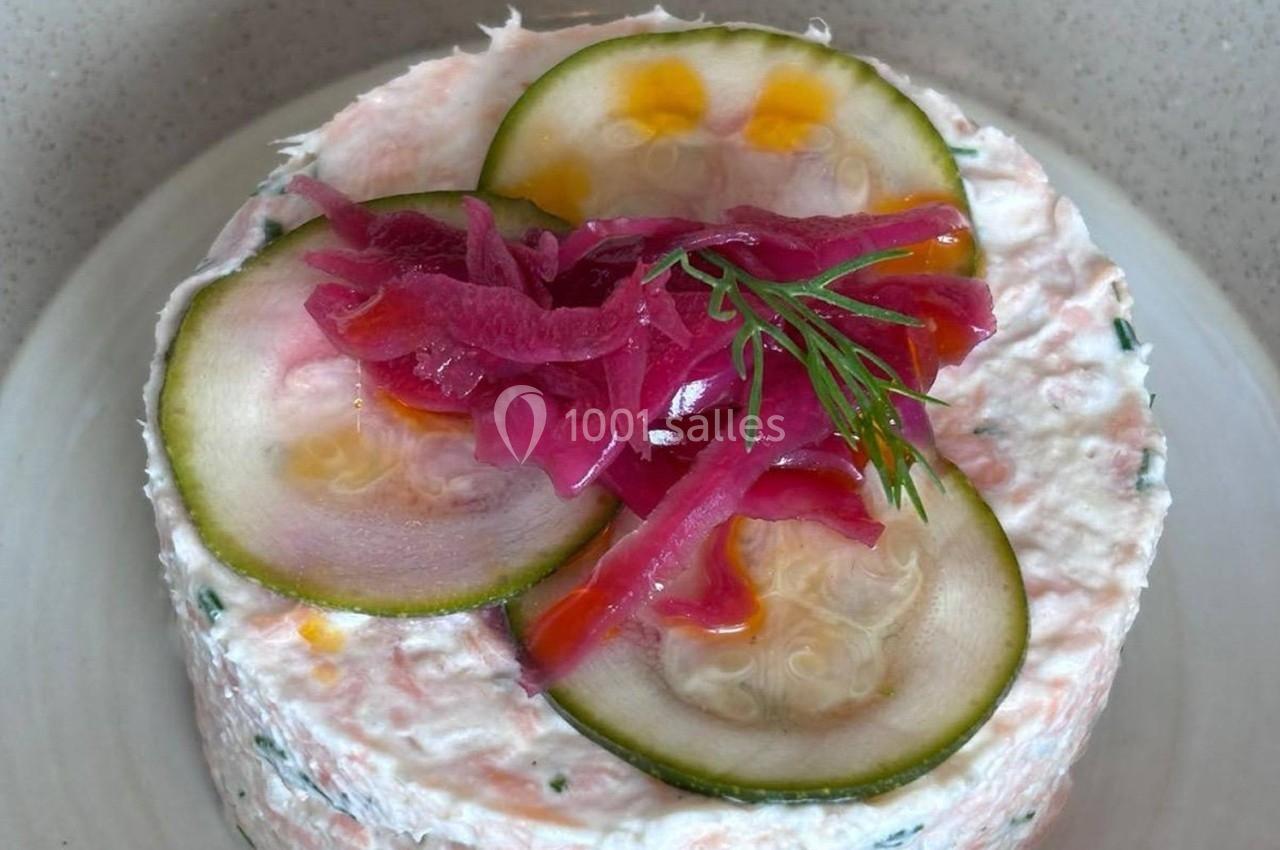 Terrine de poisson garnie de rondelles de concombre, oignons rouges marinés et brin d'aneth sur une assiette blanche.