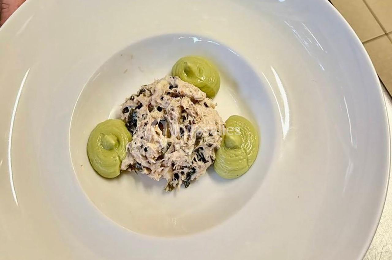 Une assiette contenant une préparation à base de poisson et d'herbes, accompagnée de trois points de purée verte.